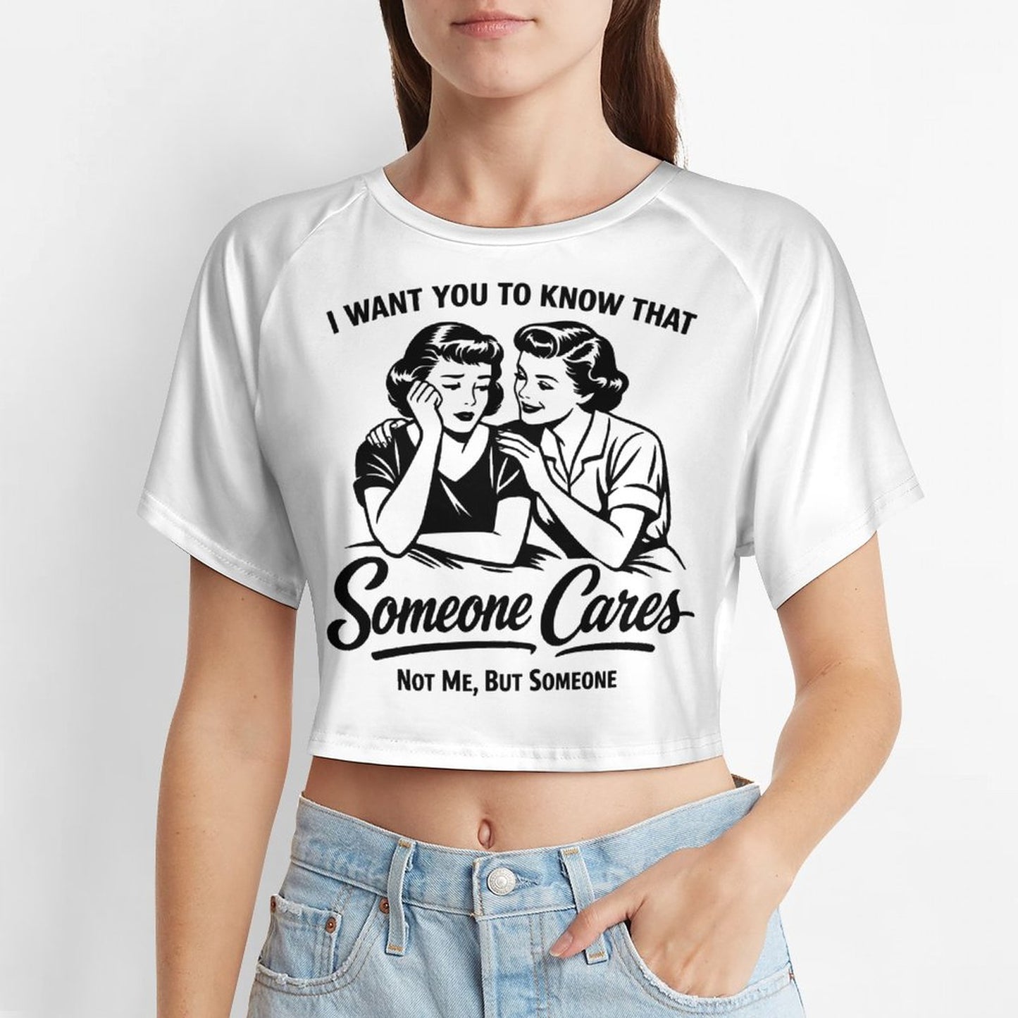 A young woman wearing a fitted white short sleeve baby tee crop top featuring a black vintage pop-art graphic of two women and the sarcastic quote I WANT YOU TO KNOW THAT Someone Cares NOT ME, BUT SOMEONE.