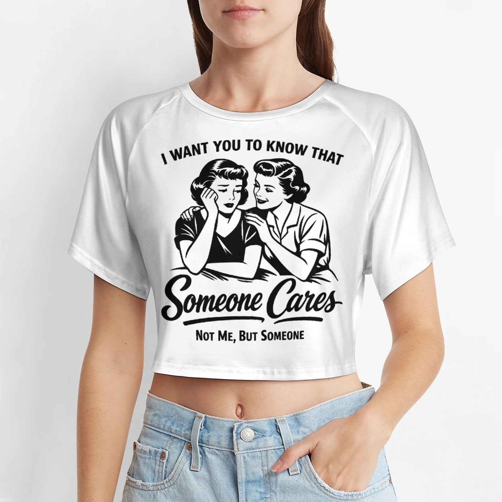 A young woman wearing a fitted white short sleeve baby tee crop top featuring a black vintage pop-art graphic of two women and the sarcastic quote I WANT YOU TO KNOW THAT Someone Cares NOT ME, BUT SOMEONE.