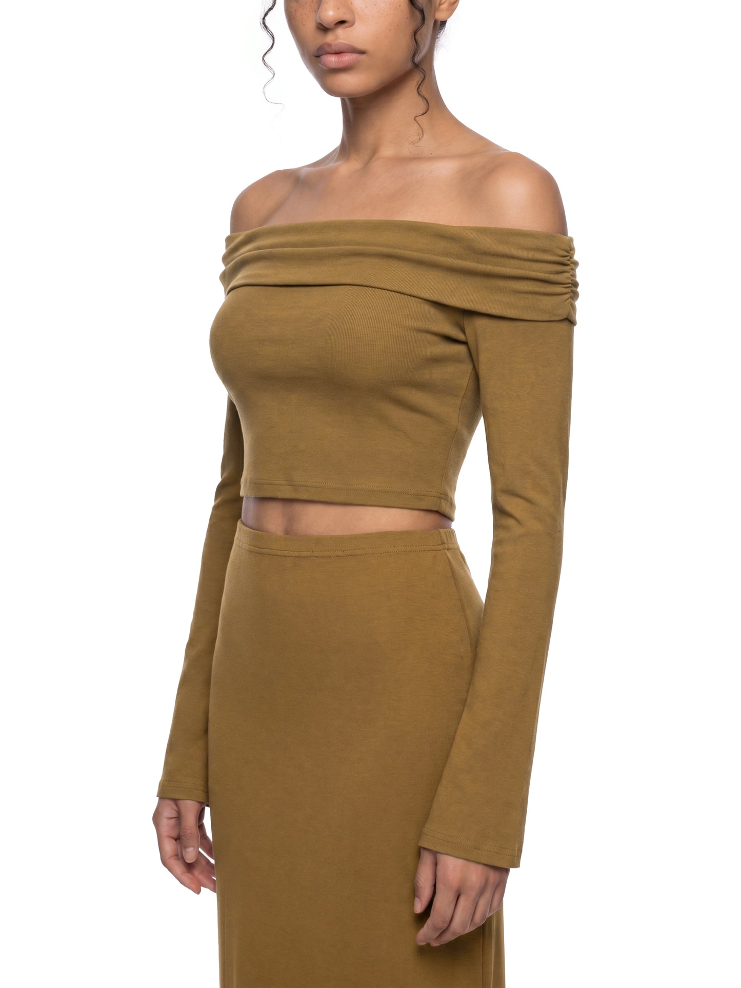 Side view of a model wearing the brown version of the BTS Arirang off-the-shoulder crop top, highlighting the form-fitting back panel and premium long sleeve tailoring.