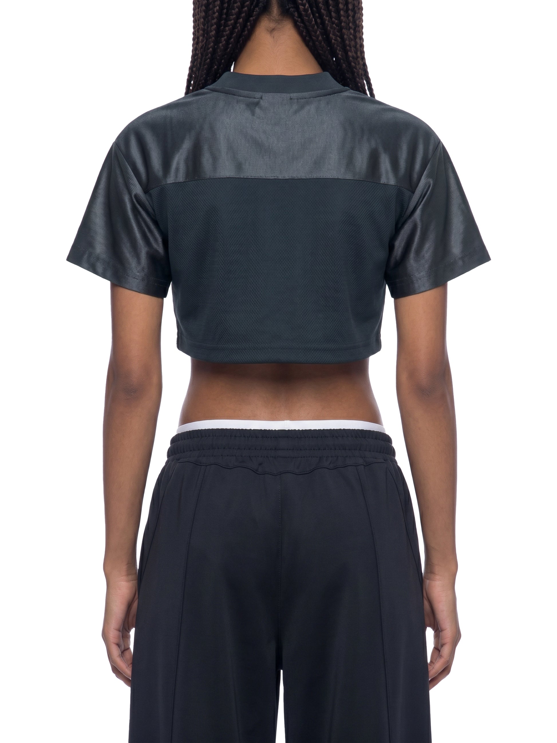 Person wearing a dark green cropped top and black pants on a white background