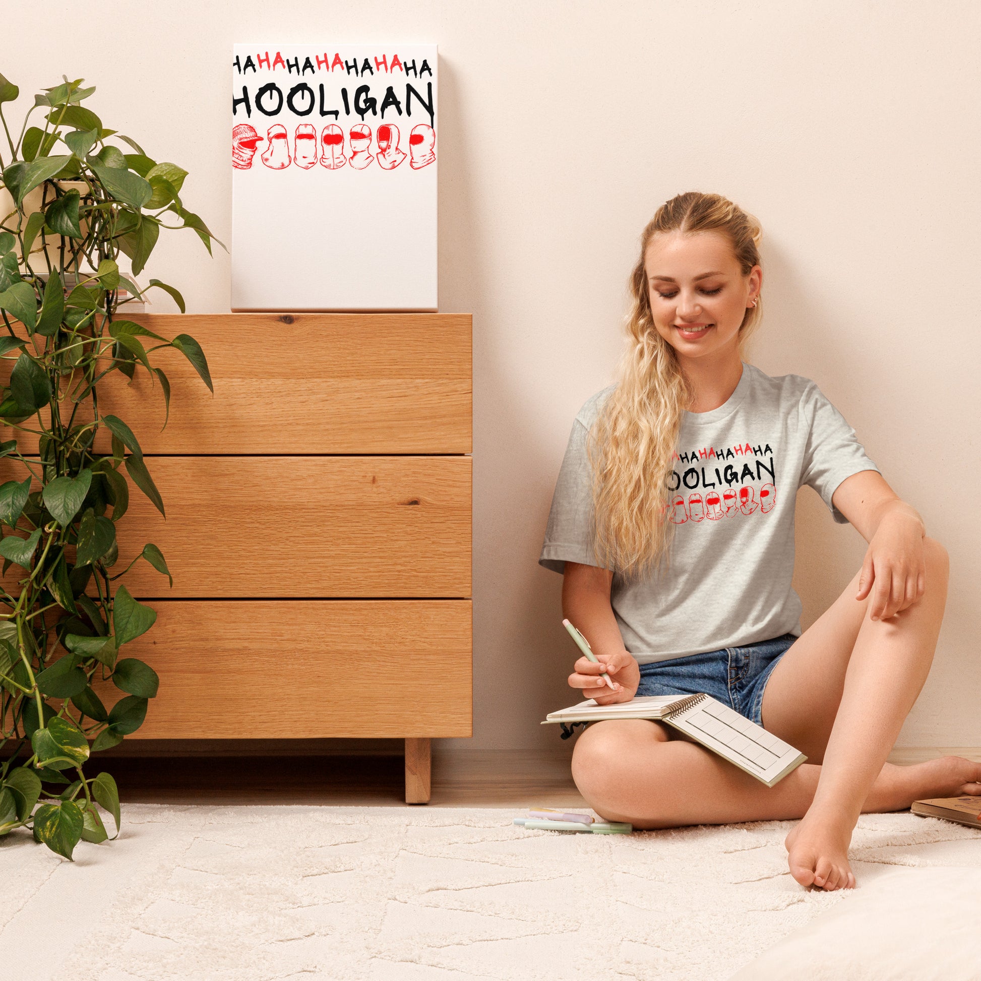 Model wearing the Ash gray BTS World Tour Hooligan unisex t-shirt while sitting on the floor in a casual home setting.